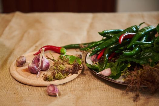 Still life with fragrant culinary herbs and ingredients for preparing brine, marinade and pickle: garlic cloves, fresh dill leaves and chili peppers on wooden board on a table with a linen tablecloth