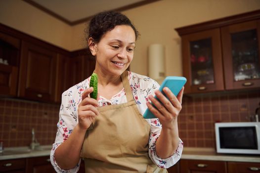 Pretty, natural beauty multiethnic woman, housewife wearing a chef's apron, looking through recipe of marinating and pickling seasonal vegetables at home kitchen. Close-up. Family traditions