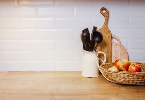 Kitchen utensils on the tabletop, vintage style culinary background, wooden planks and red fresh apples in a basket. home cooking concept. Large empty piece of white wall, copy-paste