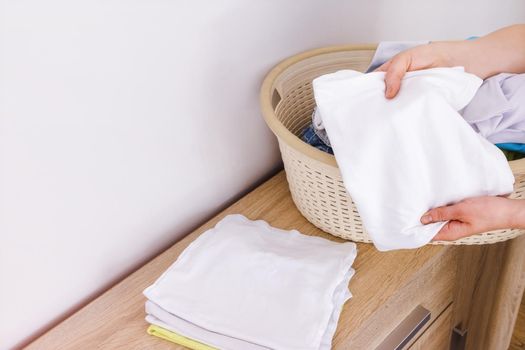 Laundry, washing powder, bleach, fabric softener. Close-up, in the hands of a woman, a clean white T-shirt close-up. Copy paste white wall background. Concept of washing, cleaning, housework