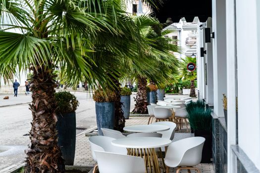 Street cafe with white chairs, green foliage around. Without people, tourism, travel
