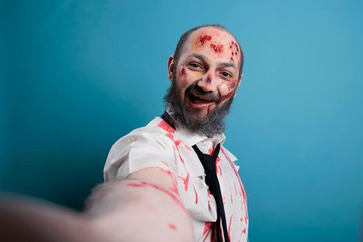 Halloween evil zombie taking photo on camera, posing in studio and looking dangerous. Brain eating corpse with bloody scars and wounds, horror aggressive monster with apocalyptic look.