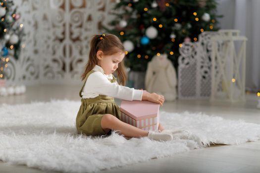 Cute kid girl holding new year gift while sitting on the white carpet.