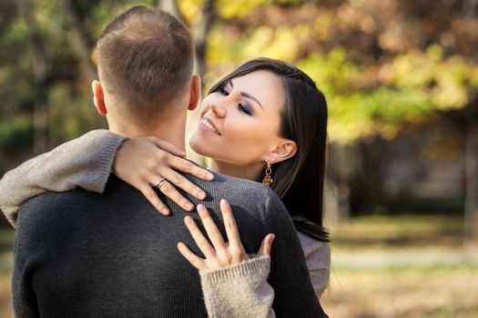 Beautiful young asian woman lovingly hugging her man in autumn park.