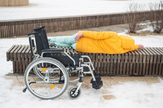 Homeless woman sleeping on a park bench next to a wheelchair