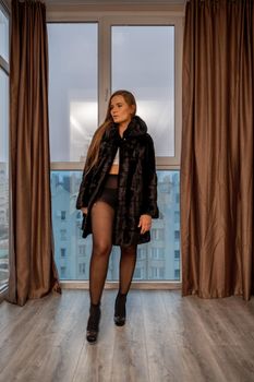 Young beautiful glamorous woman in a black luxurious fur coat posing against the background of a golden wall. fashion portrait.