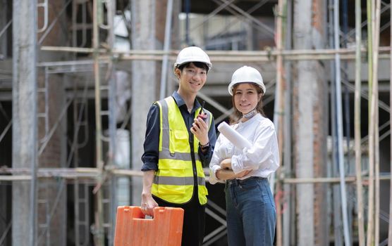 Two confident an engineers, architects or foremen standing with crossed arms pose in front of construction site as the background..