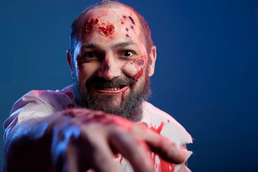 Creepy halloween zombie approaching camera in studio, looking spooky and dangerous with bloody scars and wounds. Apocalyptic sinister monster corpse with scary face and crazy eyes eating brain.