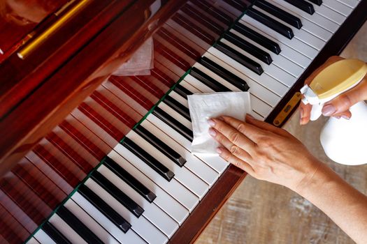 Close-up, top view. The girl's hand wipes the piano with a special liquid in a bottle. the concept of careful cleaning, caring for musical instruments. poster background