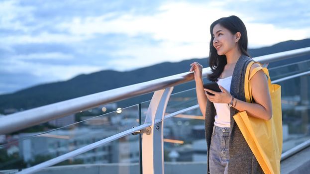 Happy young woman standing at rooftop terrace with beautiful evening sky in background.