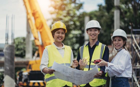 Three experts inspect commercial building construction sites and construction site holding blueprints.