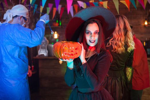 Woman with a big smile dressed up like a witch for halloween celebration. Girl holding a pumpkin.