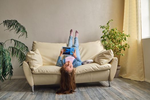 little girl lying upside down on sofa and play with tablet