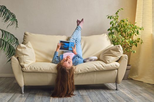 little girl lying upside down on sofa and play with tablet