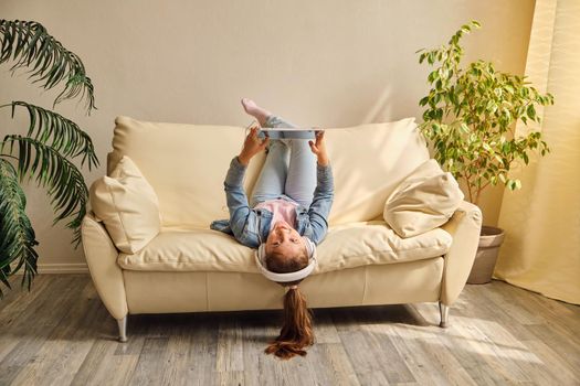 little girl lying upside down on sofa and play with tablet