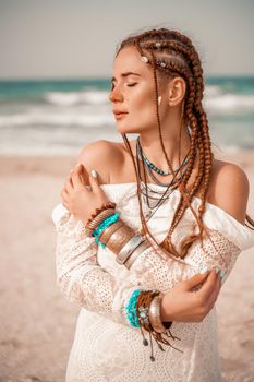 Model in boho style in a white long dress and silver jewelry on the beach. Her hair is braided, and there are many bracelets on her arms