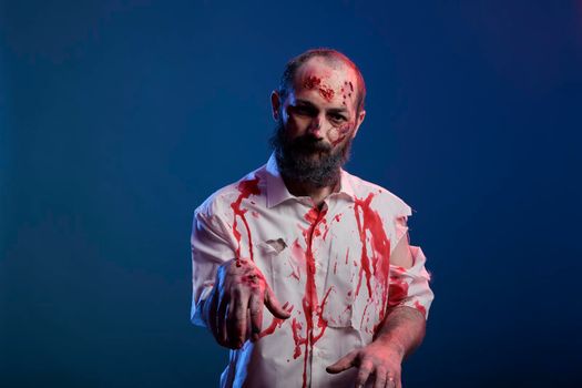 Portrait of halloween zombie with scars and bloody wounds posing in front of camera, dangerous undead corpse with scary scratches and creepy face in studio. Doomsday cruel monster devil.