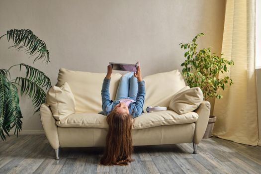 little girl lying upside down on sofa and play with tablet