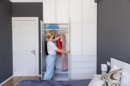 General floor plan. The girl carefully hangs the dress in the closet after dry cleaning. The concept of organizing space, order in the house, caring for things, washing, ironing. House cleaning
