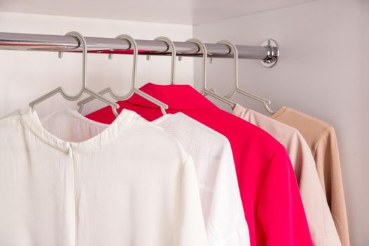 The basic wardrobe of a fashion stylist. Neutral colors: white, black, beige and accent French red. White wardrobe, gray hangers. Minimalism style