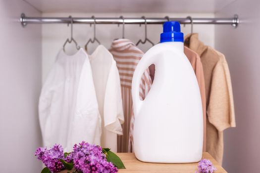 Eco Design Mockup of Empty Bottles Packing Laundry Detergent against Closet Background with Clothes in Neutral Colors. Place for text. Bio organic product. Lilac branch, fresh scent