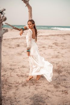 Model in boho style in a white long dress and silver jewelry on the beach. Her hair is braided, and there are many bracelets on her arms