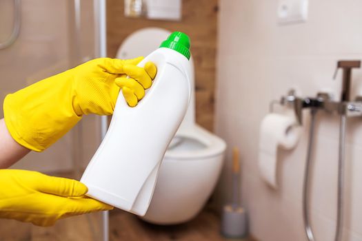 close-up, two hands in yellow rubber gloves for cleaning, hold a white bottle with liquid cleaner. Mockup for sanitary, hygienic cleaning liquid. Copy space to paste label, logo, trademark, design.