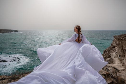 Happy freedom woman on the beach enjoying and posing in white dress. Rear view of a girl in a fluttering white dress in the wind. Holidays, holidays at sea