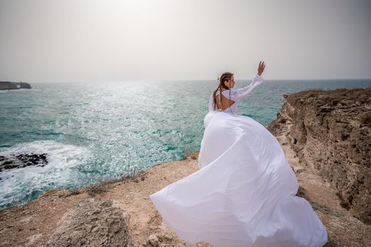 Happy freedom woman on the beach enjoying and posing in white dress. Rear view of a girl in a fluttering white dress in the wind. Holidays, holidays at sea