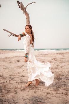 Model in boho style in a white long dress and silver jewelry on the beach. Her hair is braided, and there are many bracelets on her arms