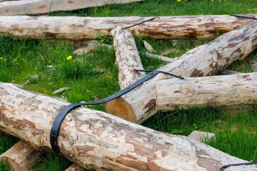 forged steel stripe connection of wooden log beams for roof support girder framework laid on green grass at summer day during assembly