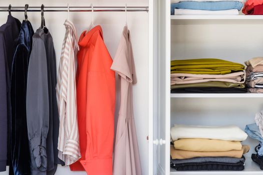 Close-up, open white closet in which blouses, dresses and jackets hang. Burdened minimalist approach to clothing selection. Working with a stylist to select a basic collection of things