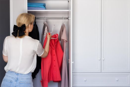 close-up, open white closet with colorful clothes. The girl hangs a pink shirt in the closet. The concept of wardrobe analysis, the work of a stylist in the selection of a basic collection of things.