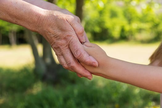 Close-up. Old wrinkled hands and young beautiful hands of a child. Care concept, different generations. Joint diseases in the elderly, diabetes mellitus, padagra, arthritis