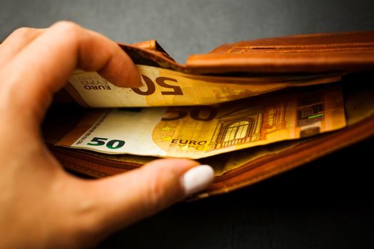 Woman's hand hand takes out banknotes from a brown wallet with euro money. Soft focus