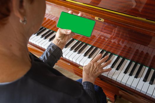 An elderly woman wants to learn how to play the piano, looks through notes on her phone. Smartphone mockup, green color key. music festival cover template, learning to play a musical instrument, top view