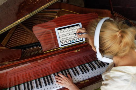 young girl composer, writes music on the tablet and plays the piano
