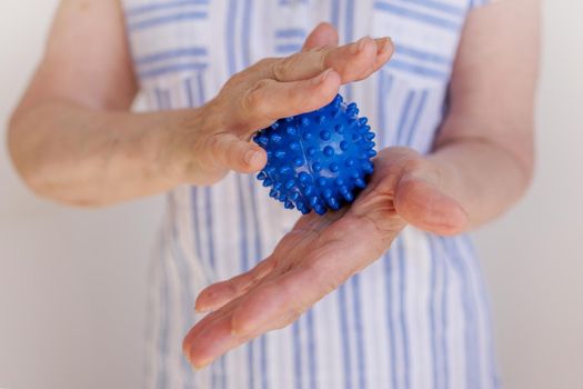 Close-up, old woman's hands massage themselves with prickly blue ball. Prevention of diseases of blood vessels and joints. The concept of treating arthritis, parkinson's disease, neurological diseases