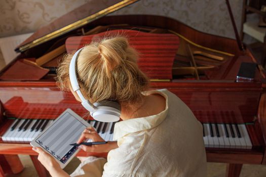 Close-up, a young girl, a blonde, composes music on the piano. Writes music to the tablet, in a special program. The concept of combining a classical musical instrument and modern technology
