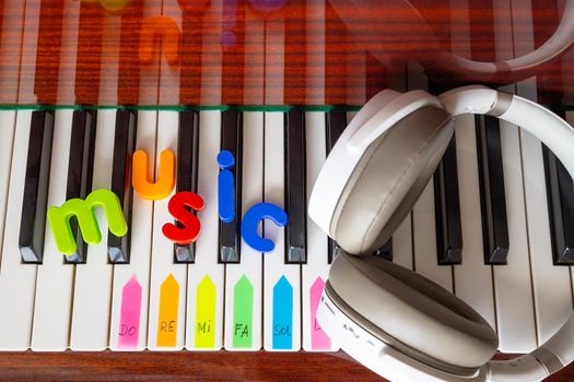 Close-up of the word music laid out on a piano from colored plastic letters. There are headphones nearby. The concept of modern and classical music, and learning through technology.