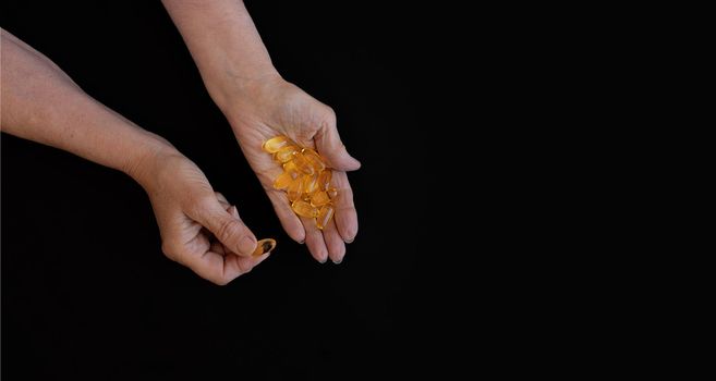 Close-up of an elderly woman's hand with a handful of Omega 3 vitamins. Black background, copy paste for your text. The concept of health prevention, taking vitamins and minerals, maintaining the body