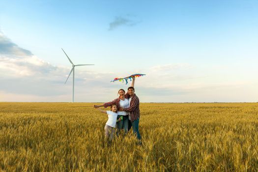 Happy family having fun with kite on the field. Beautiful family with flying colorful kite over clear sky. Free, freedom concept.