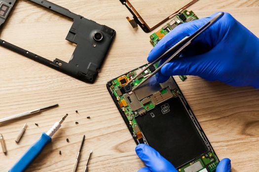 The technician repairing the smartphone's motherboard in the workshop on the table. Concept of mobile phone, electronic, upgrade and technology.