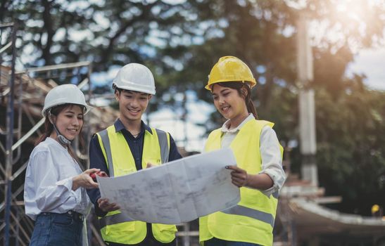 Three experts inspect commercial building construction sites and construction site holding blueprints.