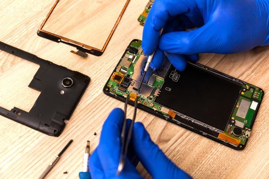 The technician repairing the smartphone's motherboard in the workshop on the table. Concept of mobile phone, electronic, upgrade and technology.