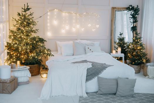 Embellished mirror, a large bed and a living Christmas tree with lights. New year's interior in bright colors, festive atmosphere, decor, garlands, gifts.