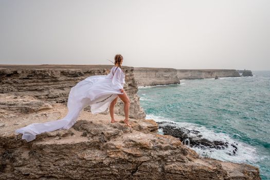 Happy freedom woman on the beach enjoying and posing in white dress over the sea. View of a girl in a fluttering white dress in the wind. Holidays, holidays at sea