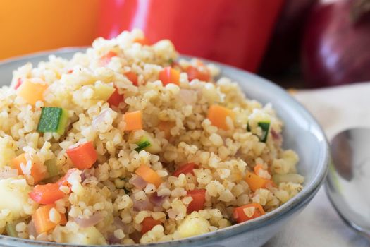 Bowl of vegan bulgur pilaf with carrots, red peppers, onions and zucchini.