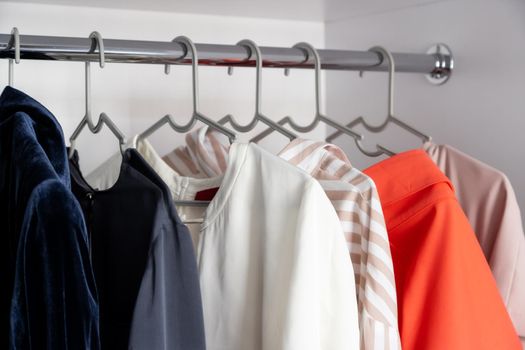 Colored clothes hang on a hanger in a home closet or store. Shirts, blouses, jackets, different colors. The concept of a clothing store, the work of a stylist in the selection of clothes