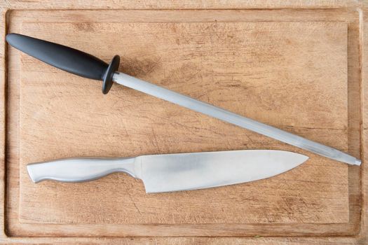 Knife and honing steel on cutting board as seen from above.